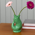 Green fish-shaped vase with two flowers on a wooden surface