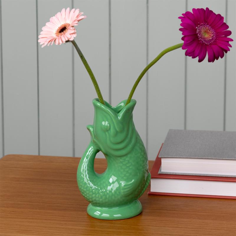 Green fish-shaped vase with two flowers on a wooden surface