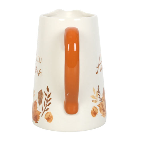White pitcher with orange handle and autumn-themed designs on a white background