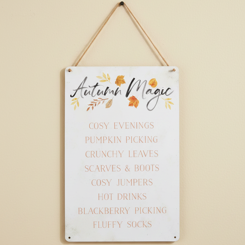 Decorative sign with 'Autumn Magic' text and fall-themed phrases on a beige wall.