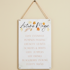 Decorative sign with 'Autumn Magic' text and fall-themed phrases on a beige wall.