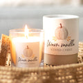 Warm vanilla scented candle with a pumpkin label on a woven surface next to its packaging
