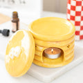 Yellow pancake shaped ceramic wax warmer with a lit candle on a white surface