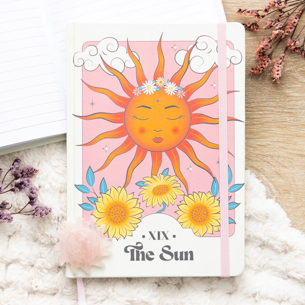 Notebook with a sun design and 'The Sun' card text on a soft surface with flowers.