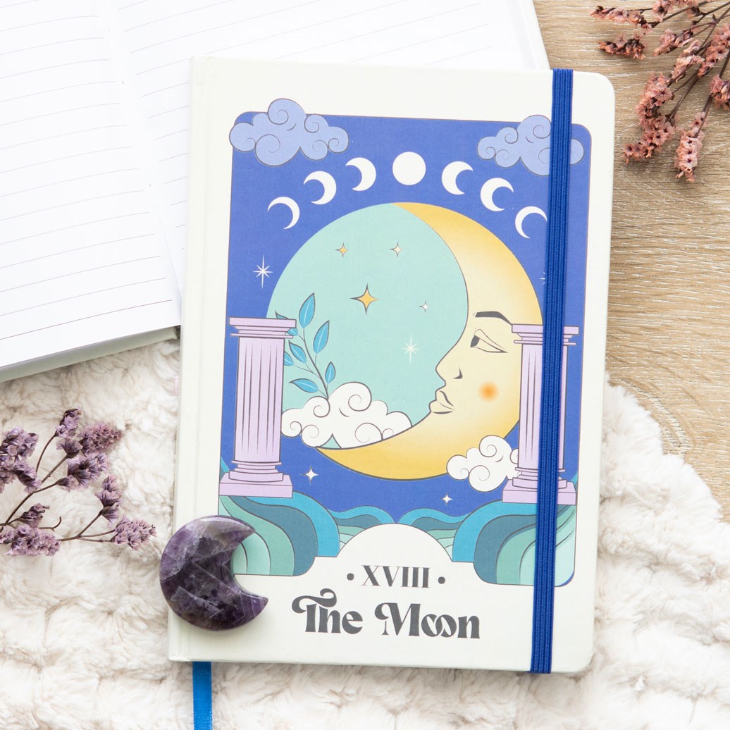 Notebook with celestial design on cover, featuring a moon and star illustration, on a soft surface with flowers.
