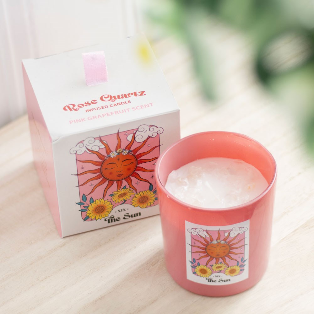 Pink candle with 'The Sun' design next to its packaging on a light wooden surface.