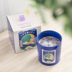 Blue candle with crystal chips with decorative 'the moon' label next to its box on a wooden surface