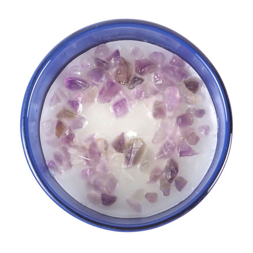 Candle with purple crystals in a blue glass on a white background
