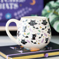 white rounded Mug with black cat and bat pattern on a notebook