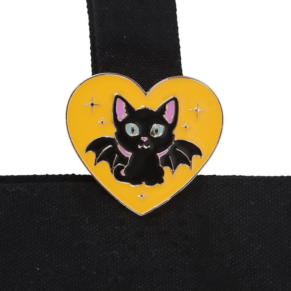 Heart-shaped pin with a black cat design on a yellow background, attached to the tote bag.