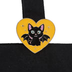 Heart-shaped pin with a black cat design on a yellow background, attached to the tote bag.