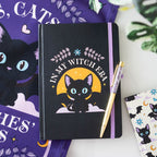 Black notebook with a cat illustration and text and a pen, surrounded by decorative items.