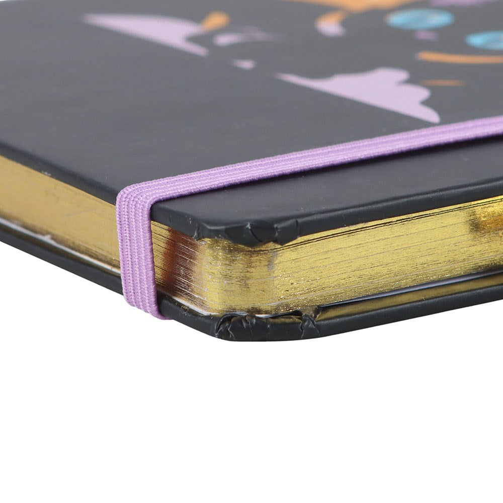 Close-up of a notebook with a black cover, gold edged pages, and purple elastic band.