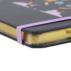 Close-up of a notebook with a black cover, gold edged pages, and purple elastic band.