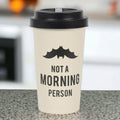 A beige travel mug with a black silicone lid and a bat silhouette design on the side, accompanied by the text 'Not a Morning Person'.