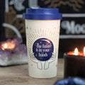 An off white bamboo eco travel mug with a navy lid and a mystical fortune teller design, placed on a wooden surface with lit candles in the background.