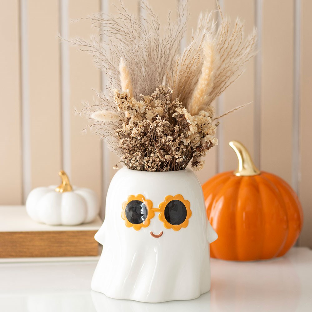 Decorative ghost vase with dried flowers, sunglasses, and pumpkins on a neutral background