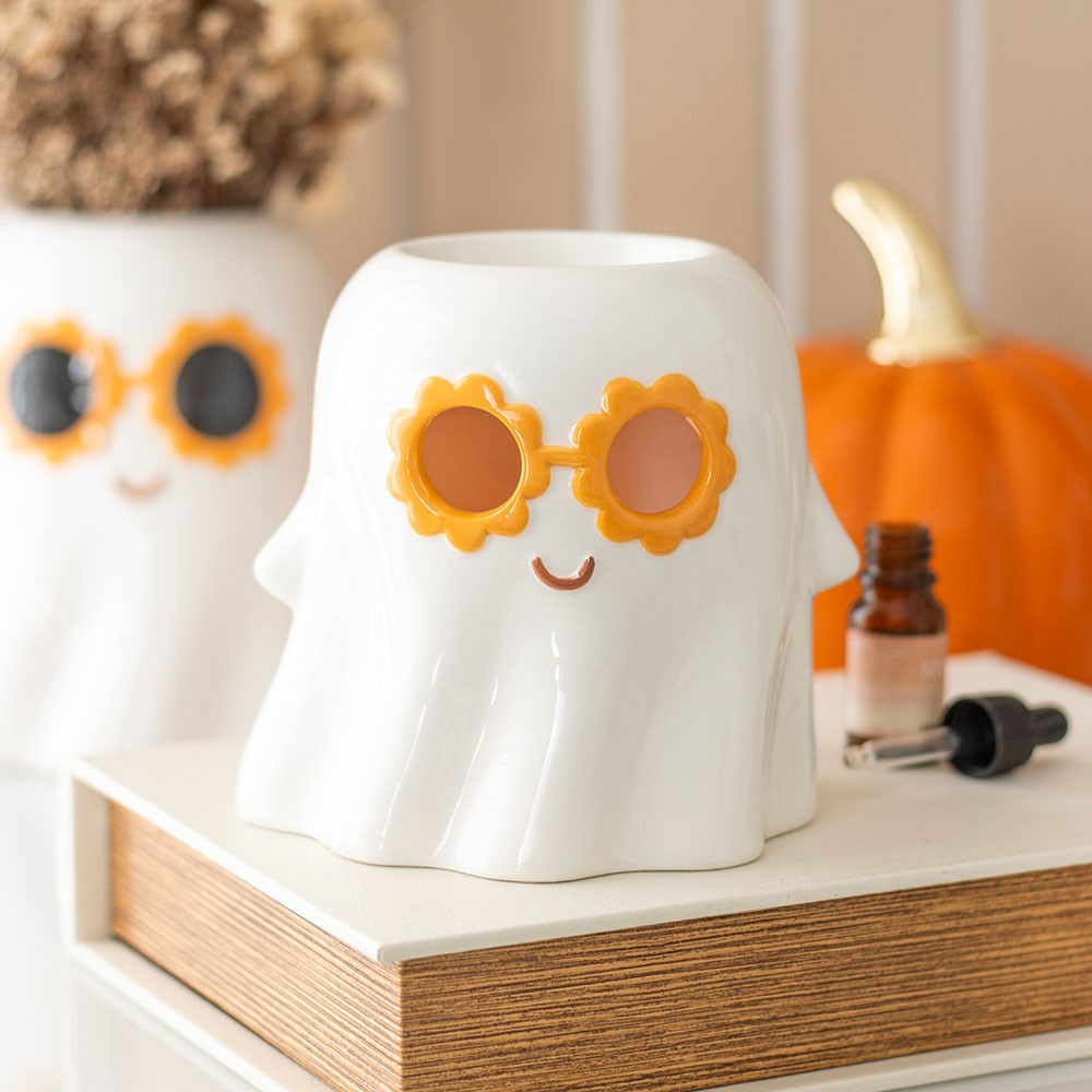 White ghost-shaped wax melt or oil burner with sunflower sunglasses on a shelf with a pumpkin in the background