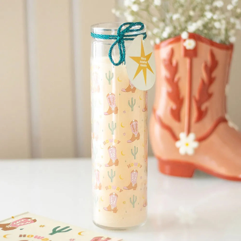 Decorative Glass Tube candle with cowboy boot and cactus pattern next to a pink cowboy boot on a white surface.