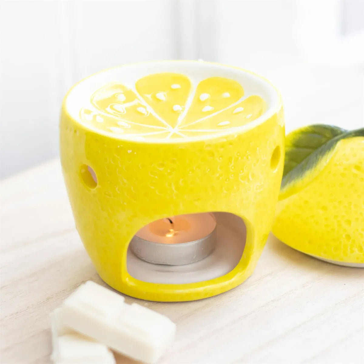 Yellow lemon-shaped oil burner with a lit tealight candle on a white background