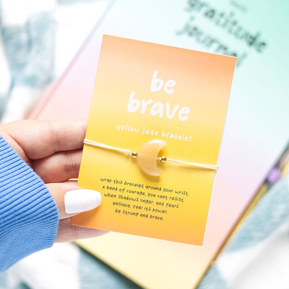 Hand holding a yellow bracelet with a 'be brave' message card.