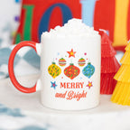 White mug with red handle featuring Christmas-themed design and text 'Merry and Bright' on a festive background.