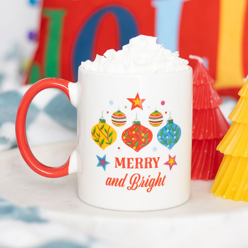 White mug with red handle featuring Christmas-themed design and text 'Merry and Bright' on a festive background.
