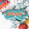 Sleep mask with retro 'Holly Jolly' text on a soft fabric background