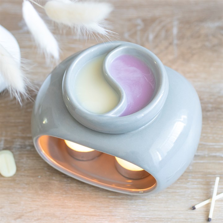 A grey double oil burner with a divided bowl for holding two different waxes or oils, with a wax warmer function, placed on a wooden surface.
