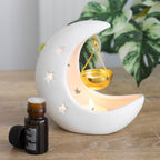 white ceramic Moon-shaped oil burner candle holder with a small bottle of essential oil on a wooden surface.