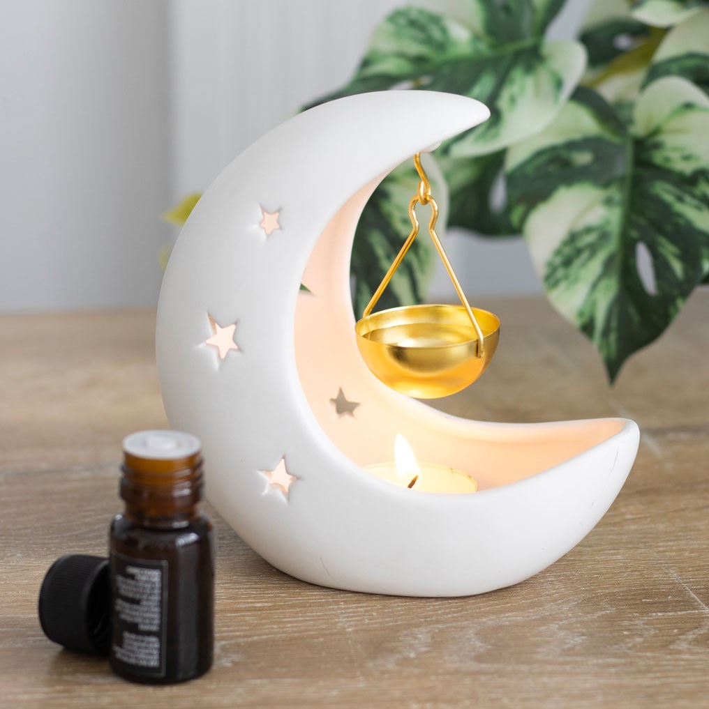 white ceramic Moon-shaped oil burner candle holder with a small bottle of essential oil on a wooden surface.