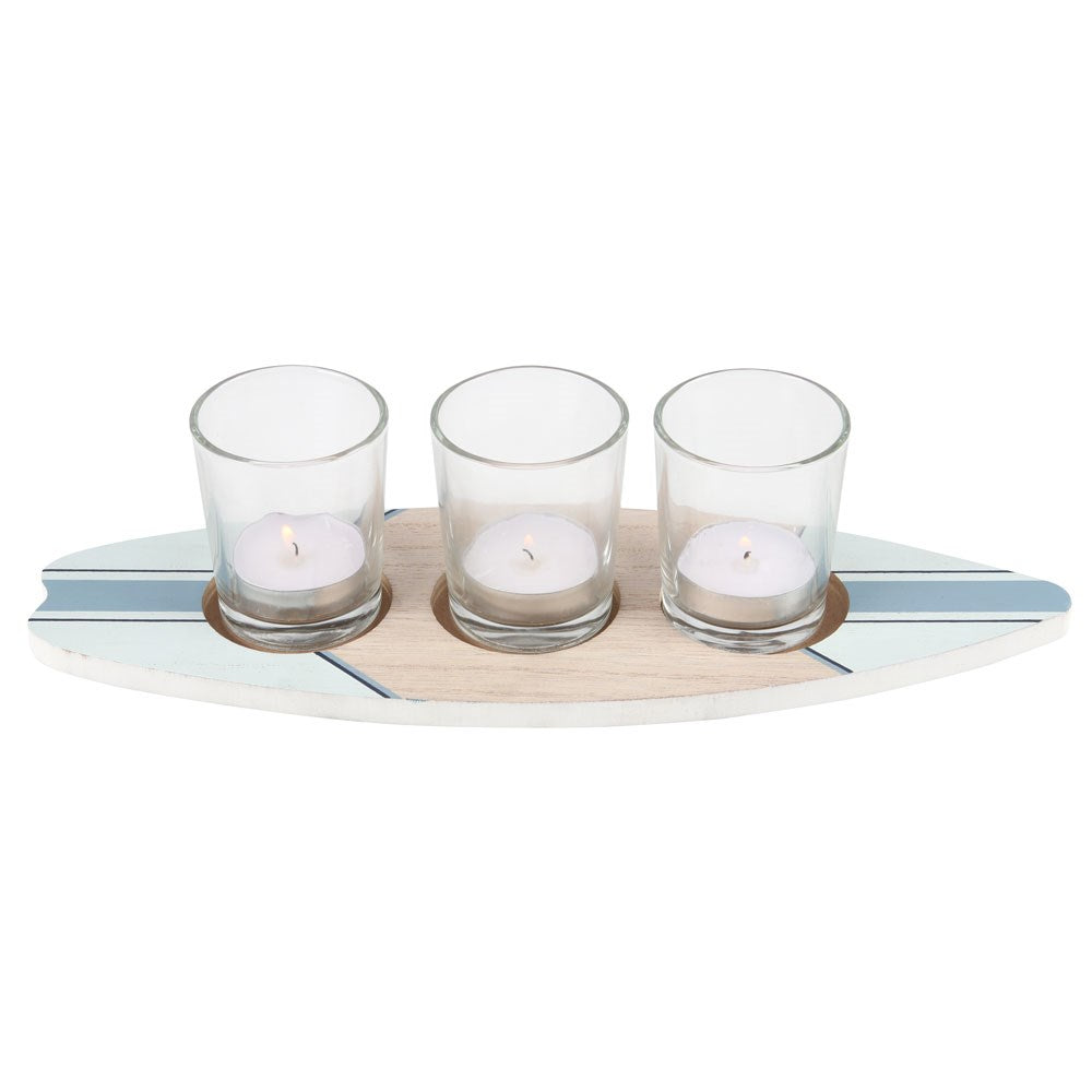 A surfboard-shaped wooden tealight holder with three clear glass holders for candles.