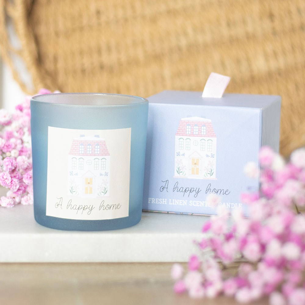 Candle with decorative packaging labeled 'A happy home' on a surface with pink flowers.
