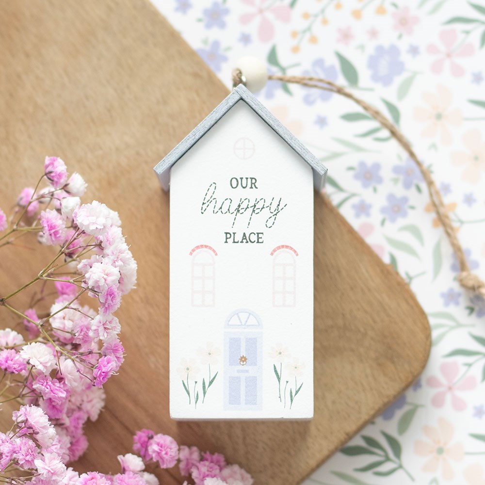 Decorative house-shaped hanging object with 'Our Happy Place' text on a floral background