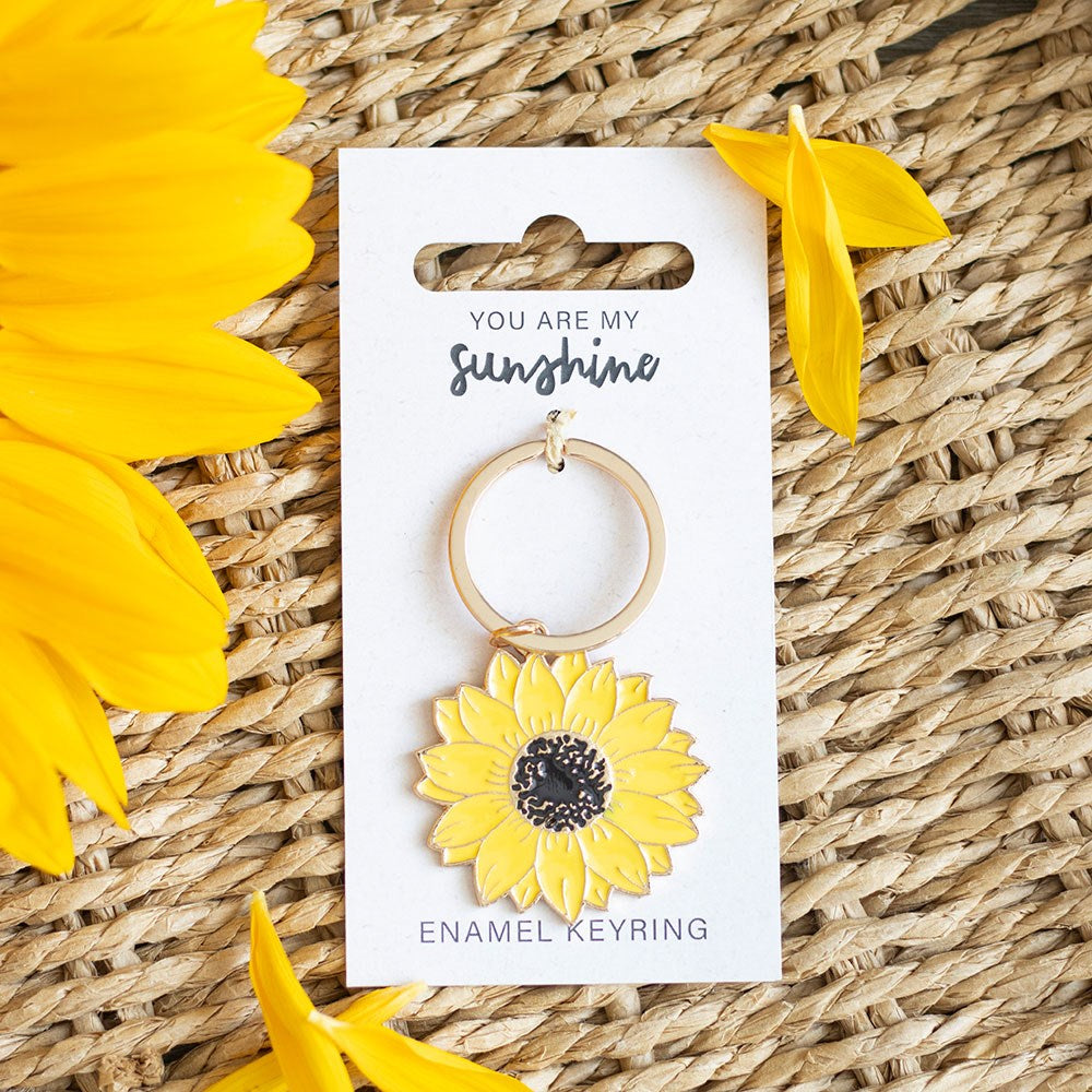 Yellow sunflower keychain on a card with 'You are my sunshine' text, surrounded by sunflowers on a woven surface.