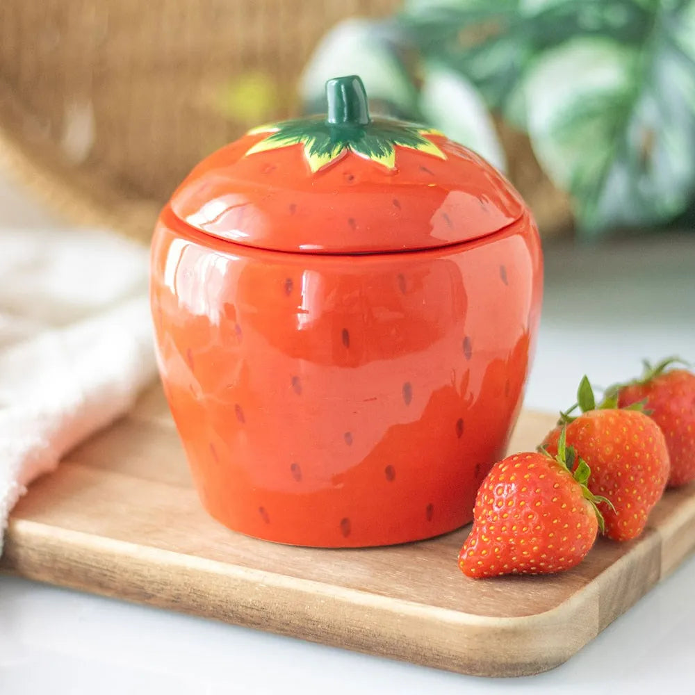 Strawberry-shaped ceramic candle on a wooden board with strawberries around