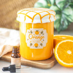 Orange marmalade-themed jar with a label, oil dropper and bottle, and half an orange on a wooden board.