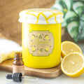 Yellow jar shaped oil burner labeled 'Lemon curd' with a dropper bottle and lemons on a wooden board.