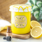 Yellow jar shaped oil burner labeled 'Lemon curd' with a dropper bottle and lemons on a wooden board.