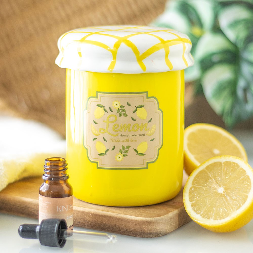 Yellow jar shaped oil burner labeled 'Lemon curd' with a dropper bottle and lemons on a wooden board.