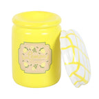 Yellow oil burner jar with a decorative label and white lid on a white background
