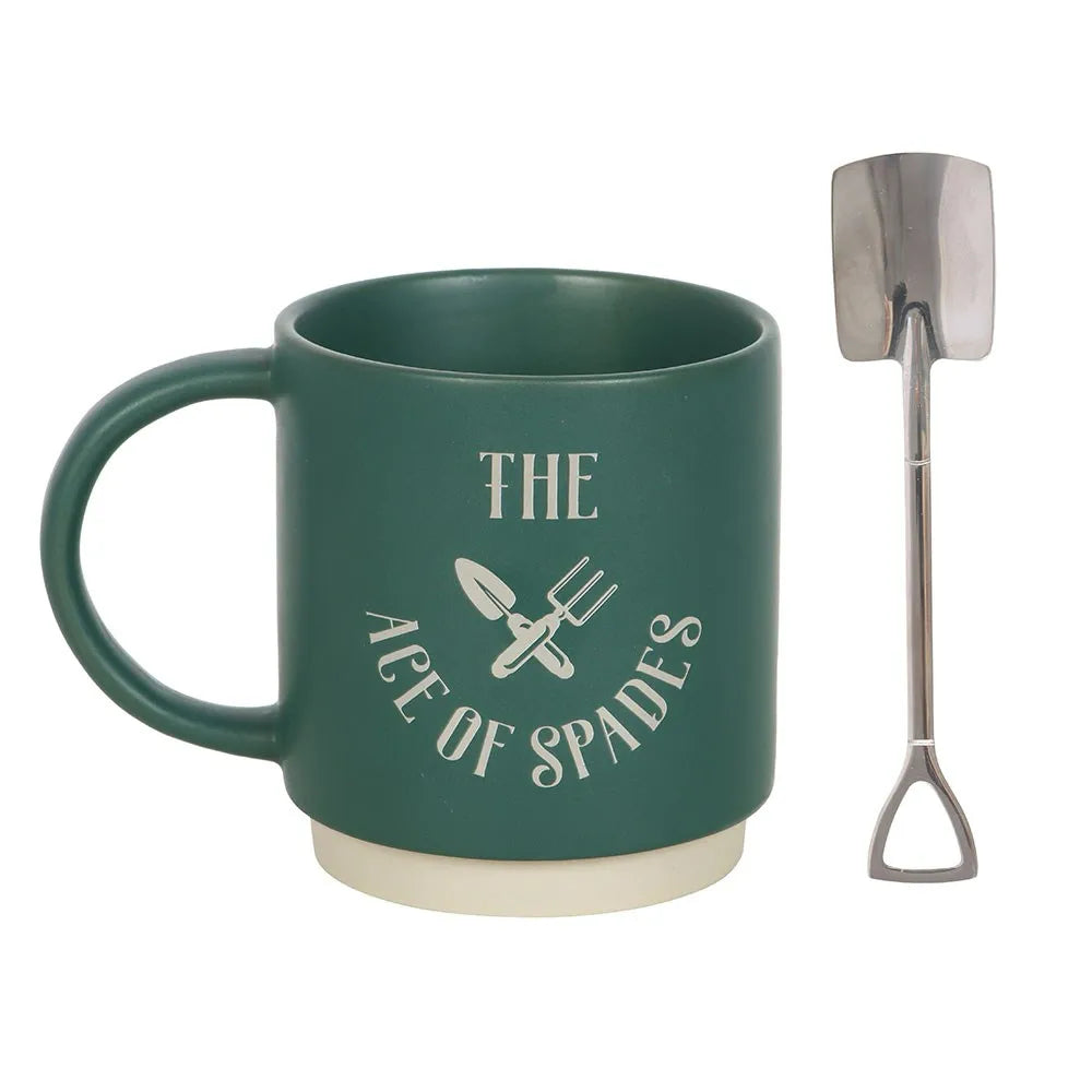 Green mug with 'The Ace of Spades' text and gardening tools, next to a small metal spade shaped spoon on a white background.