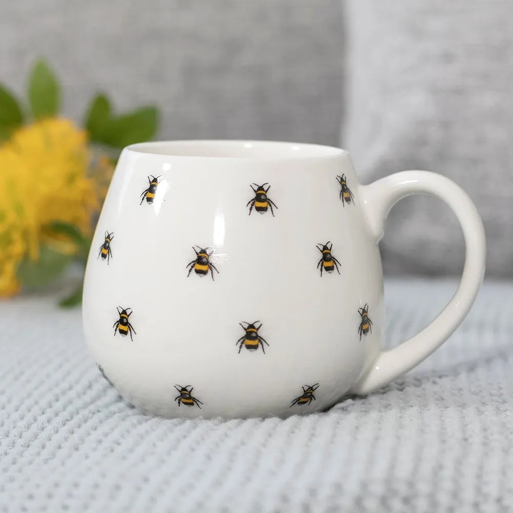 White mug with bee pattern on a textured surface with yellow flowers in the background