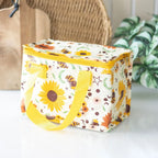 A rectangle-shaped insulated lunch bag with a cream-colored background and a vibrant sunflower and bee pattern. It features bright yellow handles and a yellow zipper