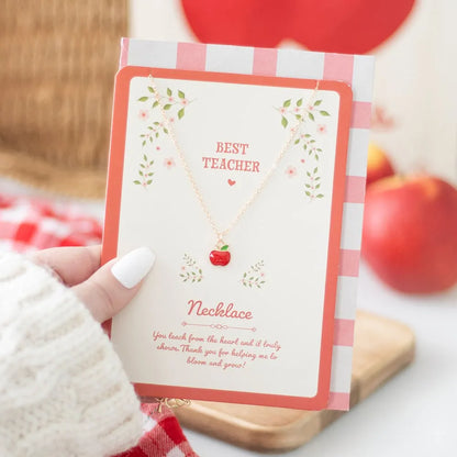Necklace on a greeting card with 'Best Teacher' text and an apple design, held by a hand.