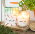 Carrot cake scented candle on a wooden surface with a plant in the background