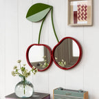 Decorative mirrors shaped like a cherry on a white wall with a vase of flowers and radio.