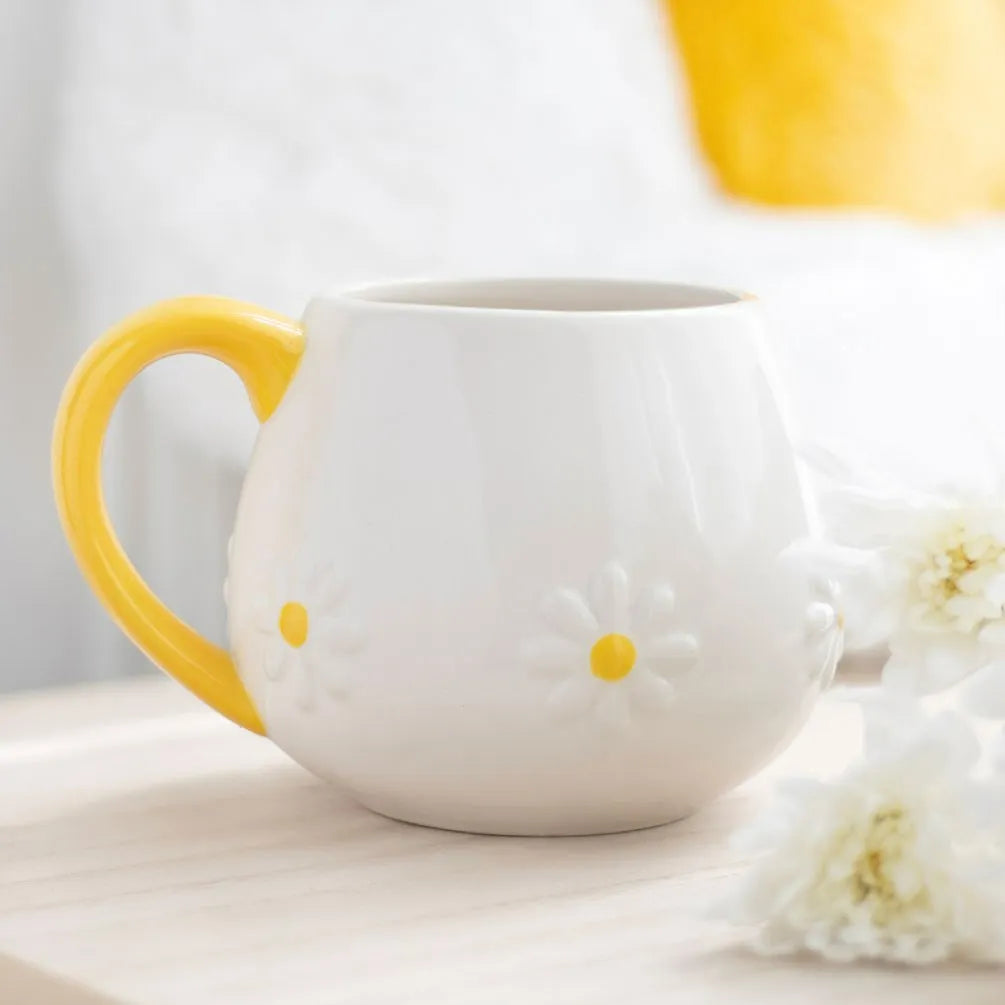 White mug with yellow handle and accents on a light surface with flowers