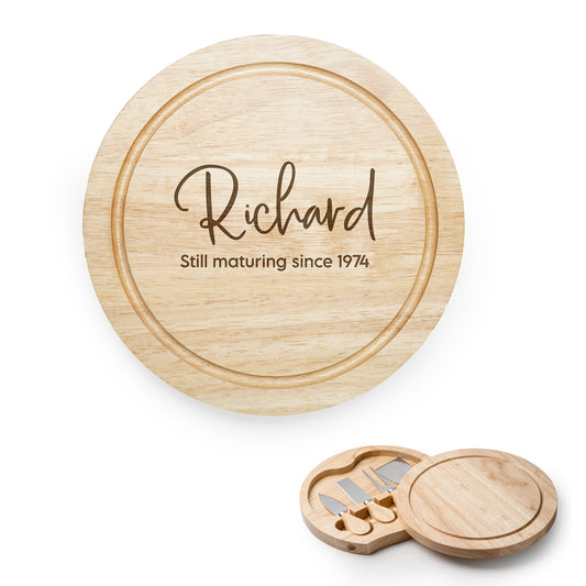 Wooden cheese cutting board with engraved text and a set of knives on a white background