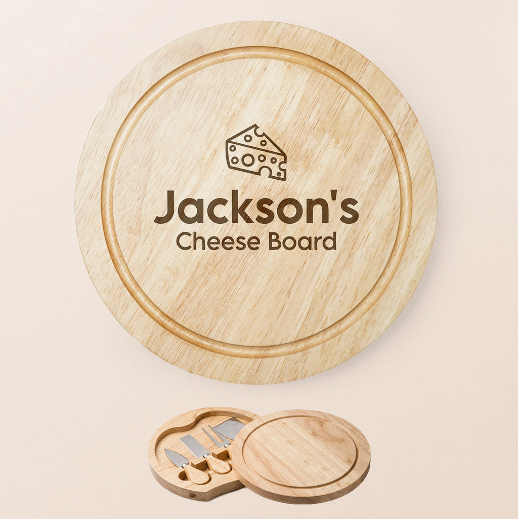 Personalized round wooden cheese board set with a matching wooden lid engraved with ''name' Cheese Board' and a cheese wedge icon, shown on a light beige background with the included cheese knife tools at the bottom.